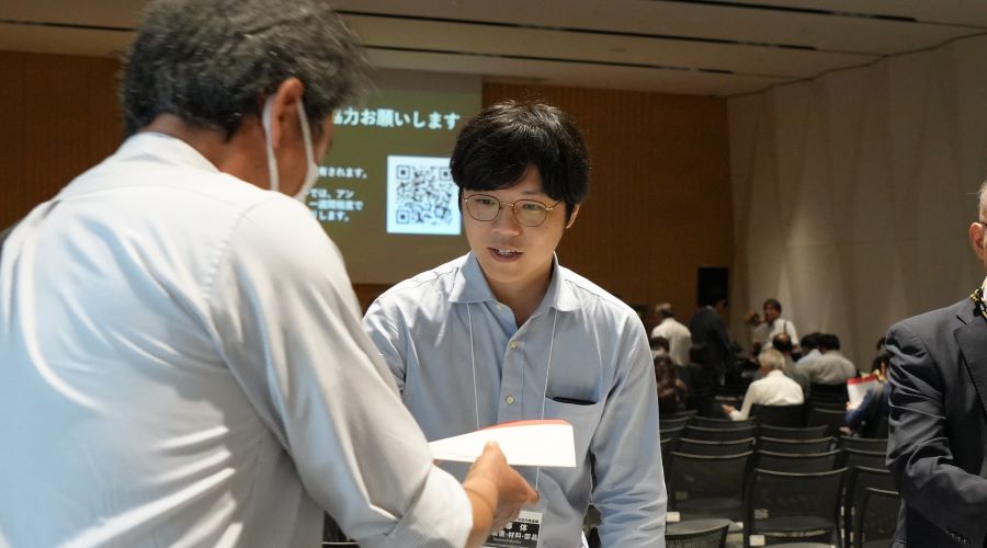 受付で資料を渡す首藤サポーターの様子
