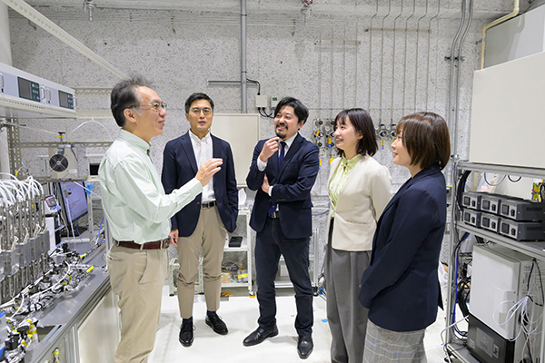 装置の前で話す5人（左から遠藤 明、牧野 貴至、河野 雄樹、白川 桃子、池田 歩）
