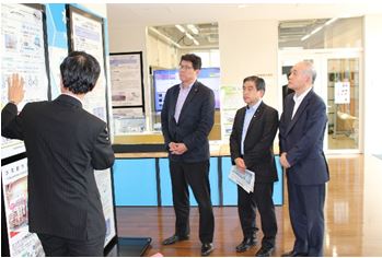 エネルギー管理棟で各研究テーマの説明をお聞きになる高木復興大臣（左から２番目）及び若松復興副大臣（左から３番目）の写真