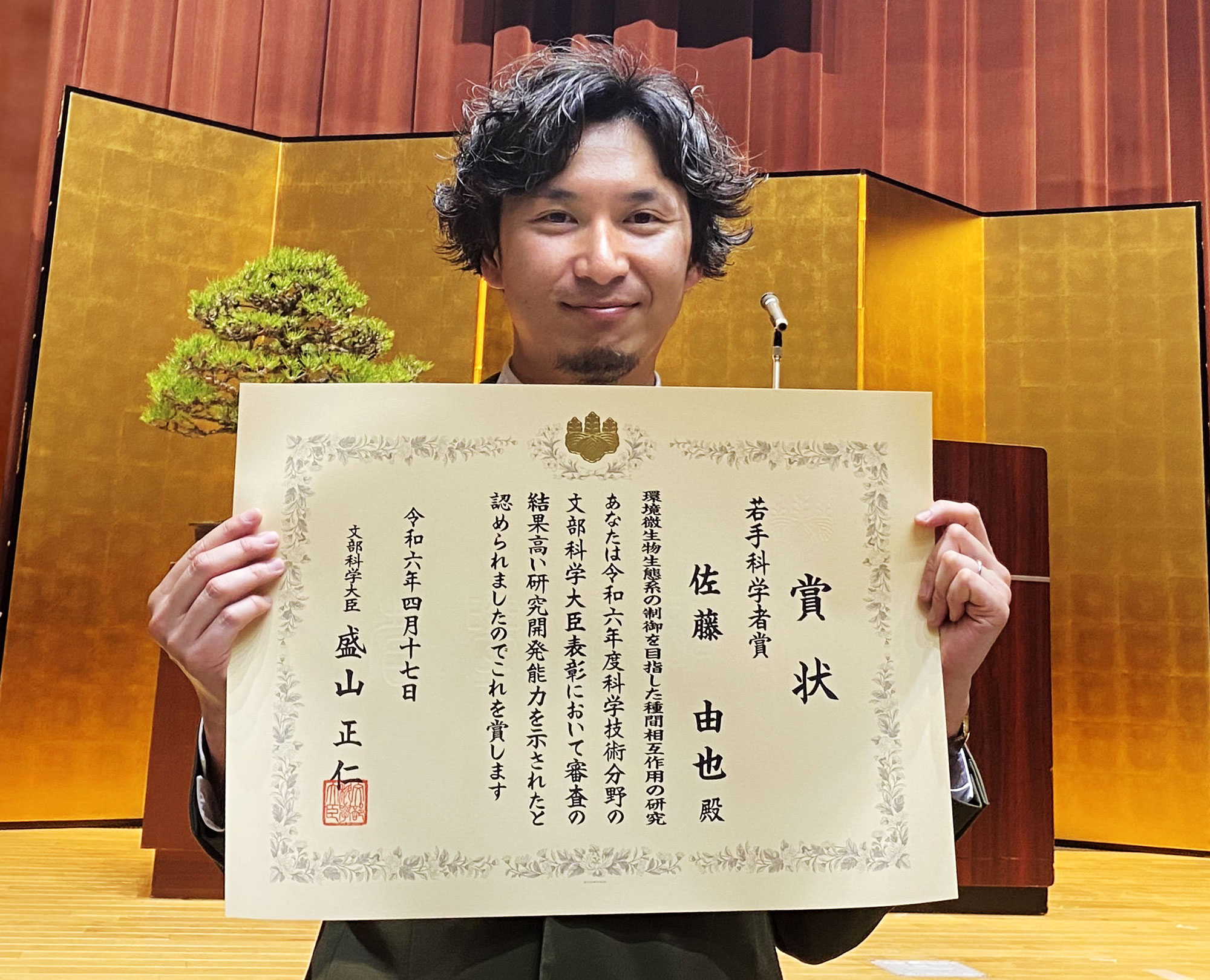 賞状を持つ佐藤由也主任研究員の写真