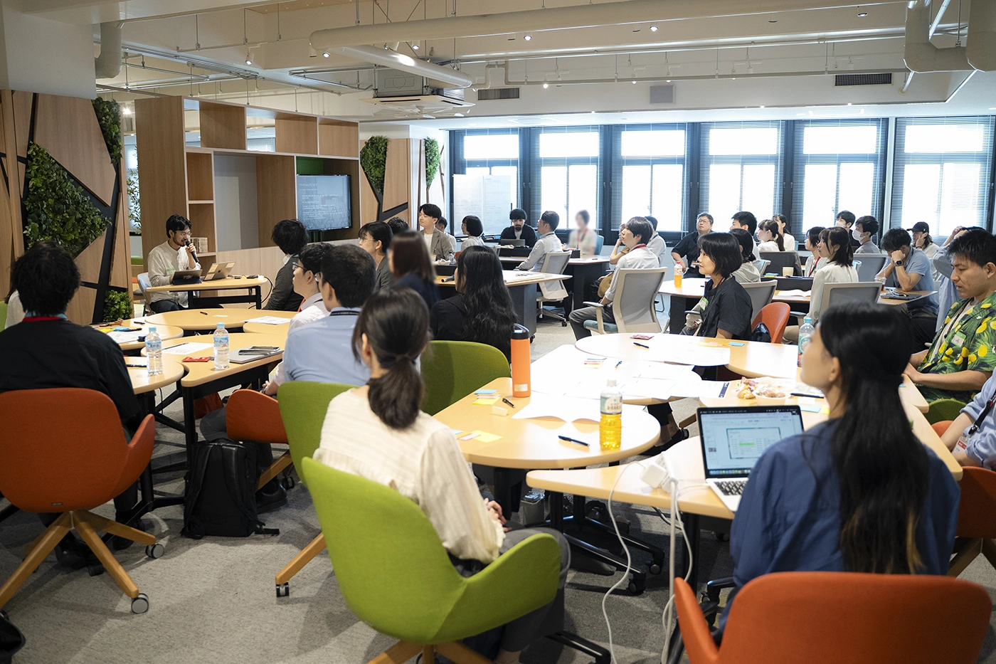 円卓を囲んで着席し、前方のモニターに視線を向ける参加者たち 